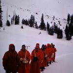 People wearing red cots and eye protection in snow