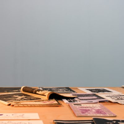 A wooden table holding zines stands in front of a blue wall