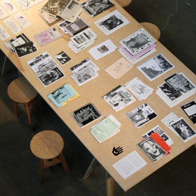 An aerial view of zines laid out on top of a wooden table with visible titles including BENDING YOUR MIND OVER and America Go Fly A Kite