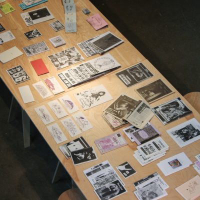 An aerial view of zines laid out on top of a wooden table with visible titles including FIX MY HEAD and LIAR and creme brulee