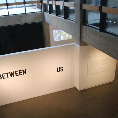 An aerial view of the gallery wall on which the exhibition title Between Us is displayed