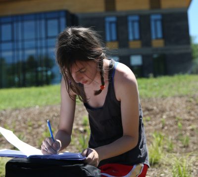 Student with brown hair in two braids makes notes in front of the R.W. Kern Center