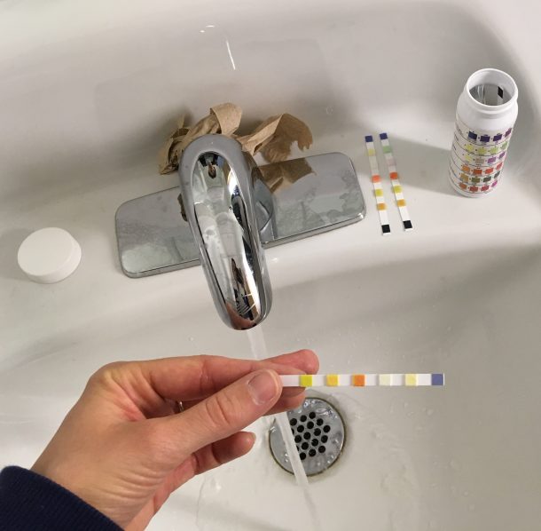 Hand holding a pH test strip over a sink.