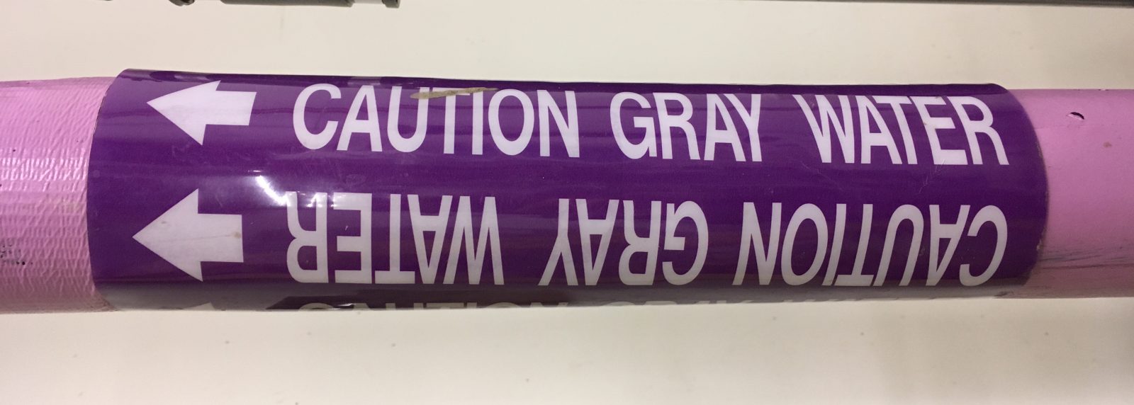 Close-up of a purpler "caution grey water" pipe.