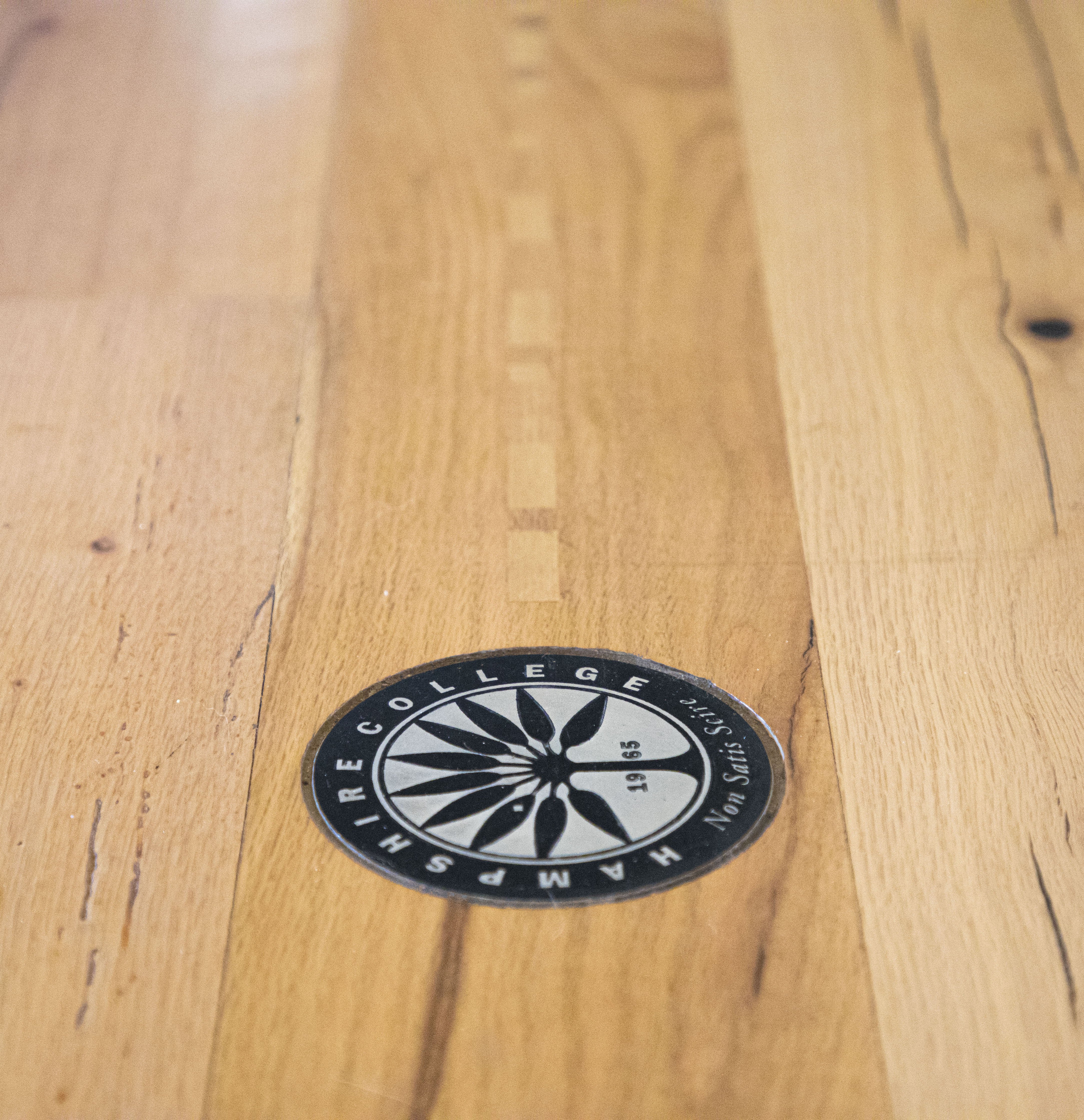 The wood floor in the R.W. Kern Center, with the black and white Hampshire College logo sticker on the floor.
