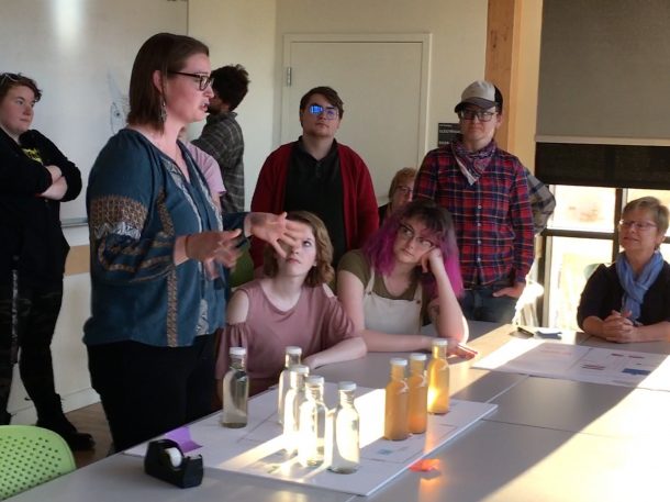 Student giving a water quality demonstration; glass bottles filled with water on the table.