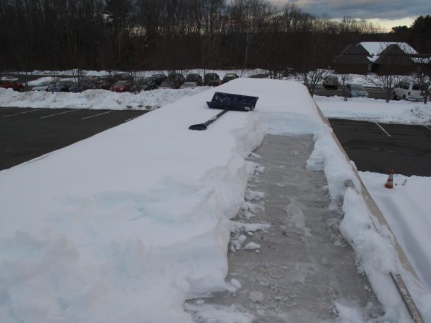 A picture of a roof covered in snow with only one line of cleared snow, the shovel lying on top of some of the snow.