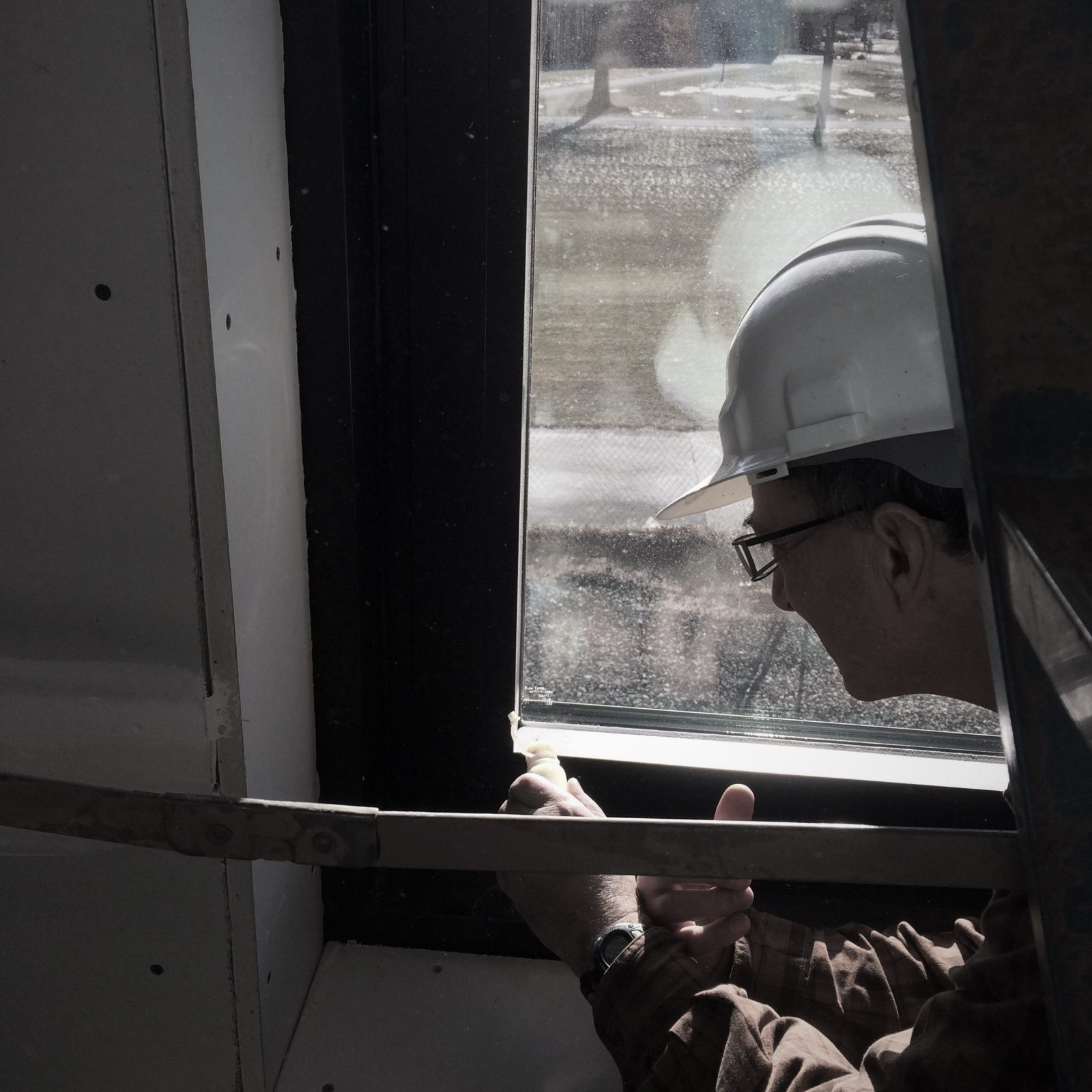 Gray tinted photo of a man in hard hat in front of a window.