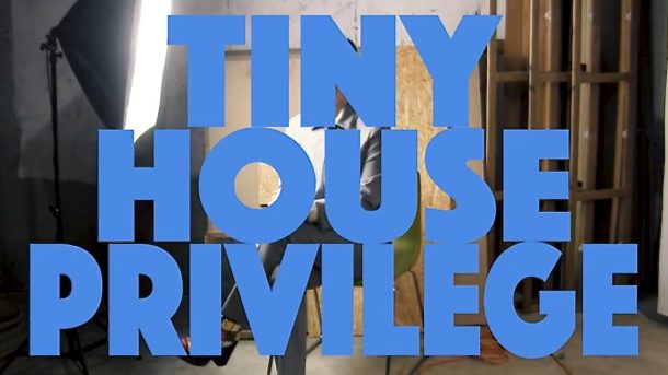 A man in an unfinished building with a photo spotlight on him. He is hidden befind blue bolded words that reads, "TINY HOUSE PRIVILEGE."