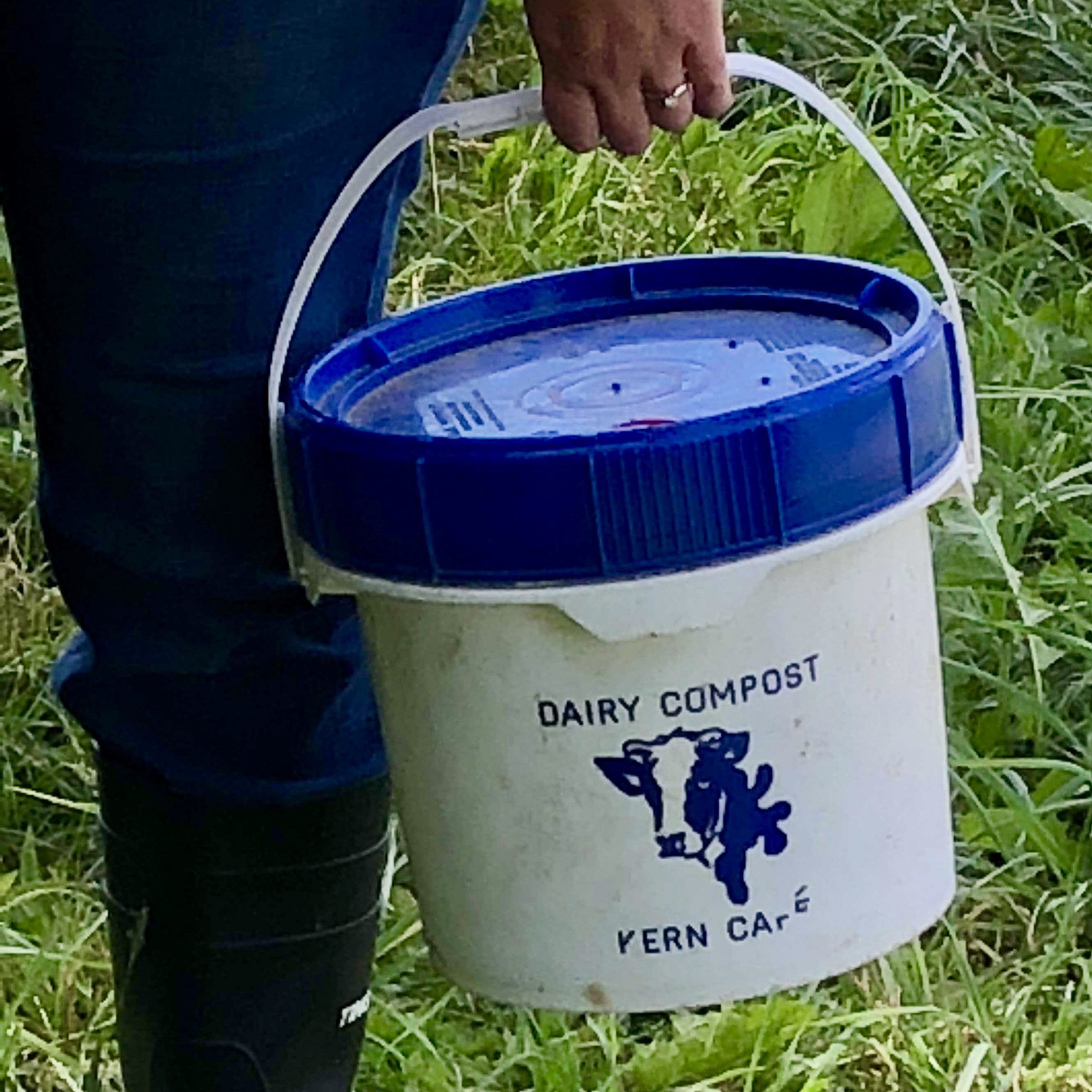 A person carrying a "Dairy Compost Kern Cafe" blue lid and white base bucket.