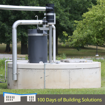 A stainless steal downspout leads to a small and large filter, all of which sits atop a large concrete cistern. The grass is green in the foreground and lush, green trees are visible in the background. A banner at the bottom of the image includes a simple shape of the R.W. Kern Center and reads: 100 Days of Building Solutions.