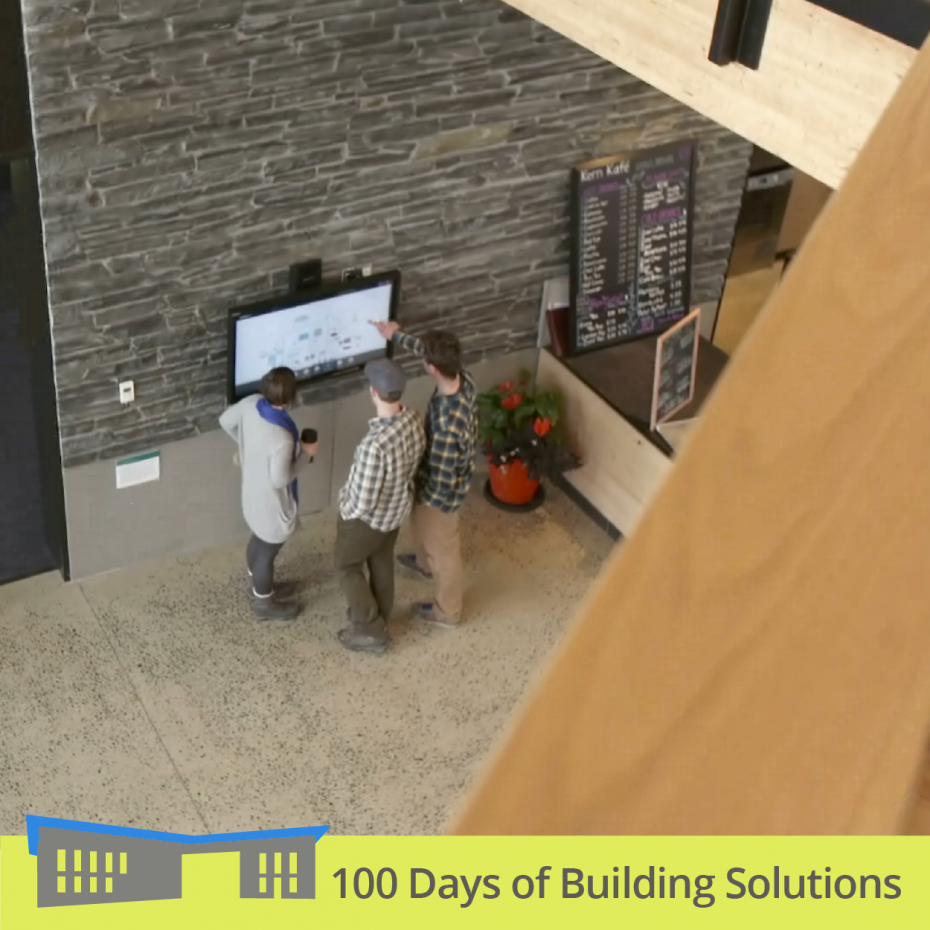 A photograph taken from the second floor of the R.W. Kern Center shows the backs of 3 people standing around a large monitor. One person points to something we can't see on the monitor. A banner at the bottom of the image includes a simple shape of the R.W. Kern Center and reads: 100 Days of Building Solutions.