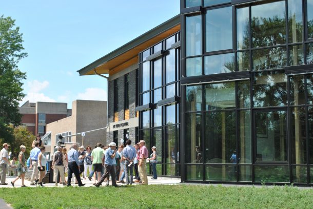 Image shows a group of people walking towards the door of the R.W. Kern Center. The sky is bright blue, and the building has a dark grey stone facade and large windows.