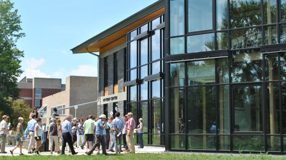 Image shows a group of people walking towards the door of the R.W. Kern Center. The sky is bright blue, and the building has a dark grey stone facade and large windows.